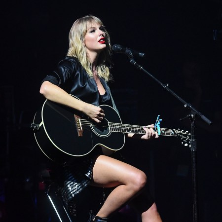 Taylor Swift in black playing a guitar at a concert
