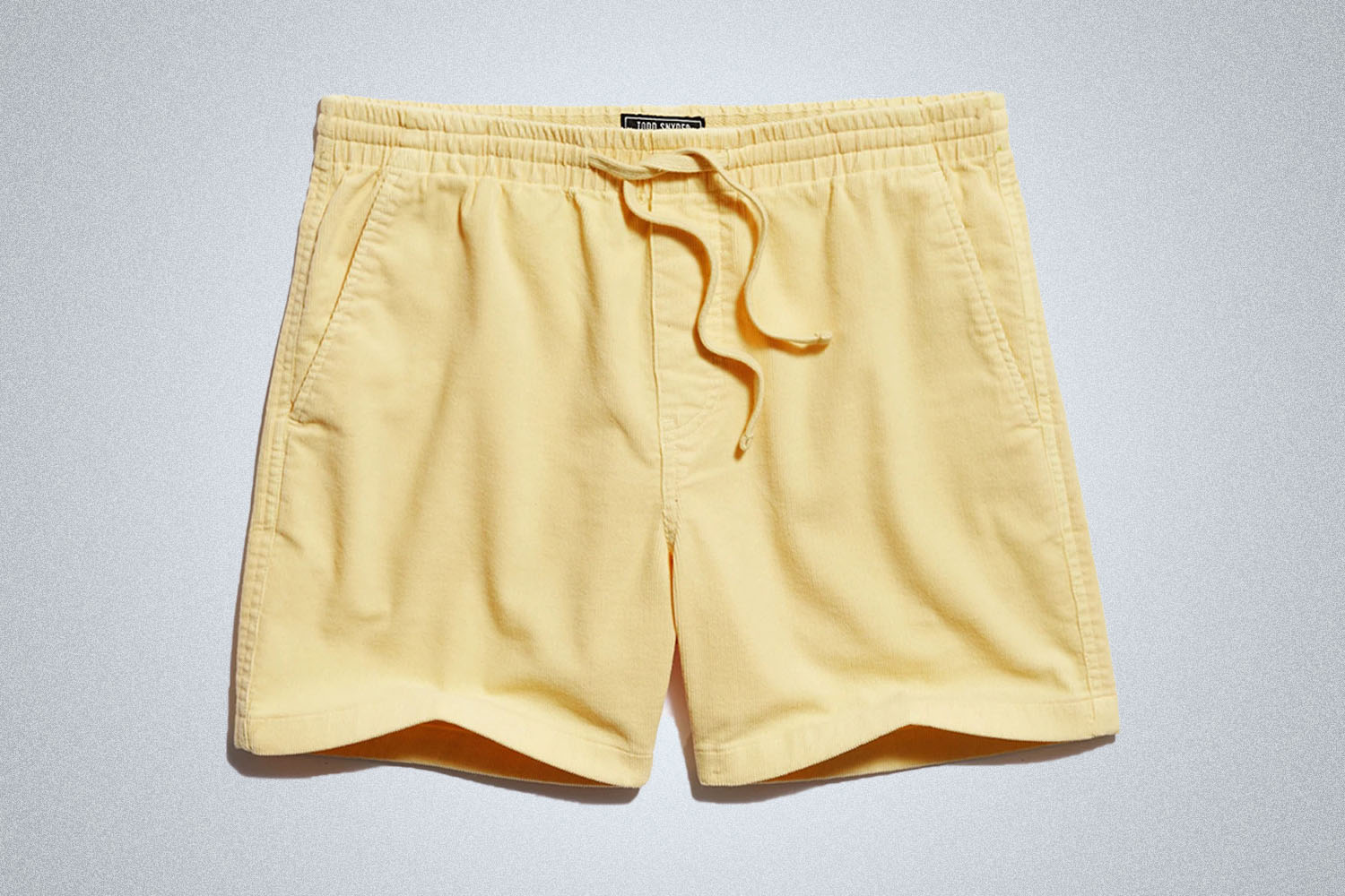 a pair of yellow Todd Snyder shorts on a grey background
