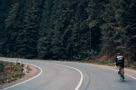 person cycling up an empty road next to a forest