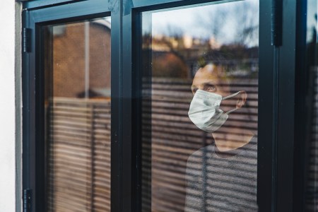 man standing behind glass in a face mask