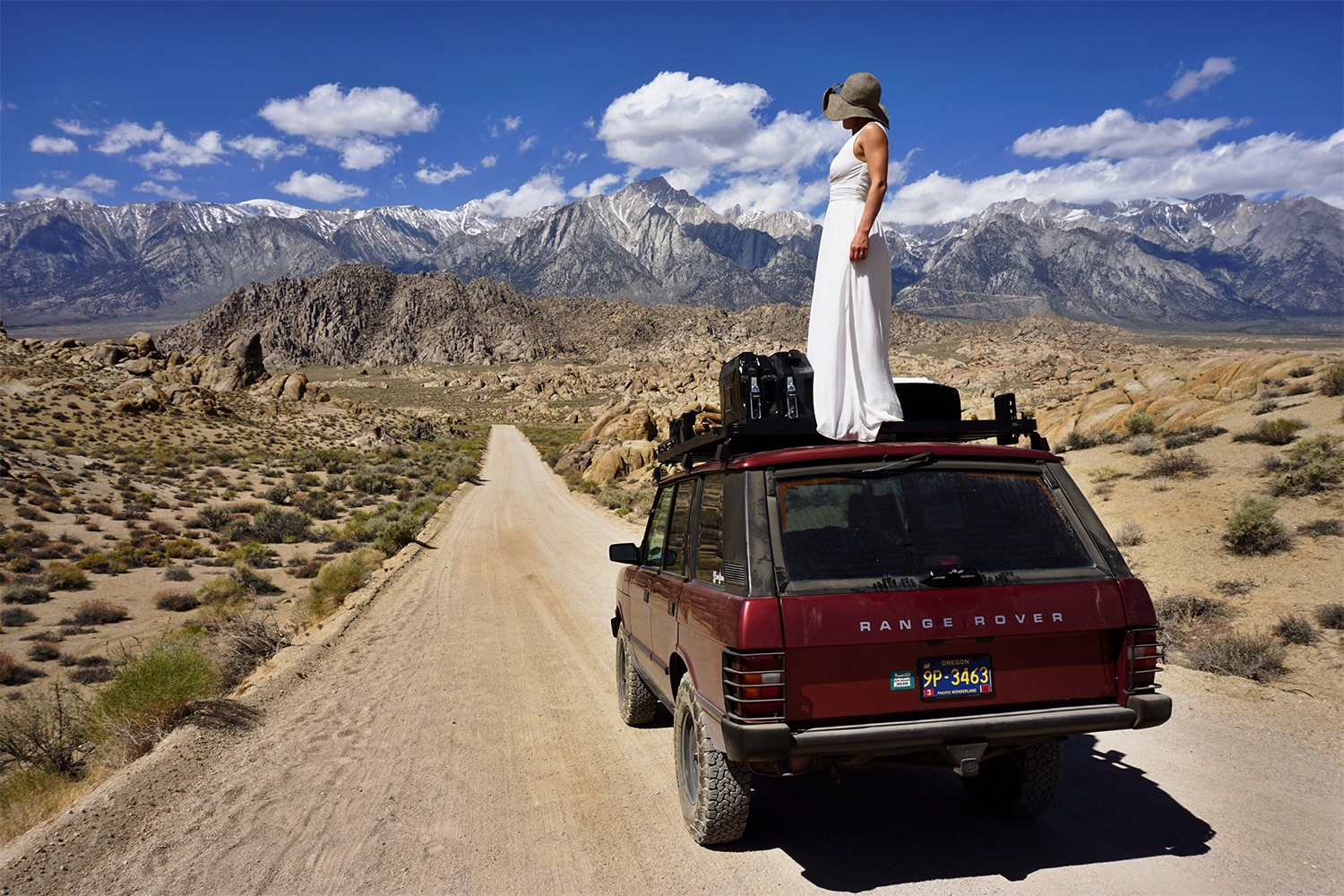 Woman in a wedding dress standing on a red 1991 Range Rover Classic SUV
