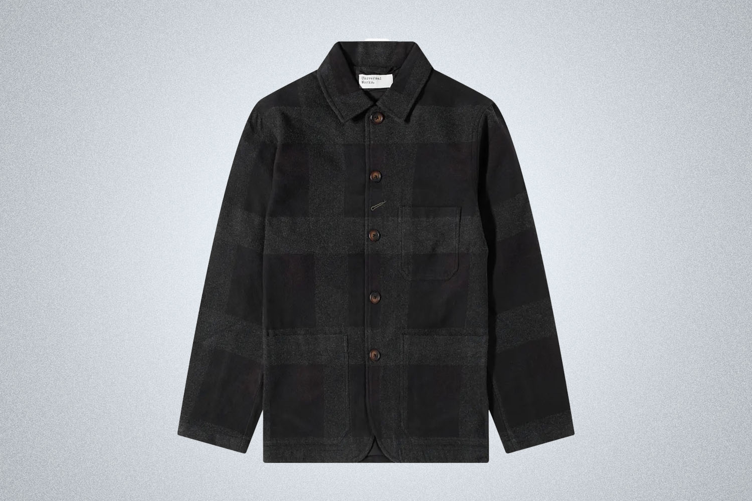 a brown flannel checked Universal Works Chore Coat on a grey background