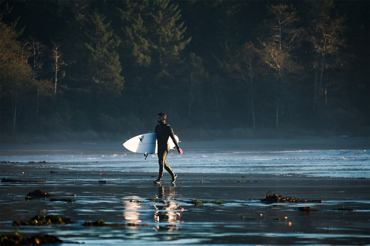 A surfer walking with a surfboard on the beach in Tofino, Canada
