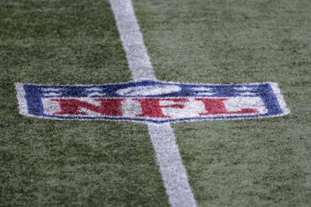 NFL logo on the field during a game between the Patriots and Raiders. NFL players have a 73% vaccination rate.