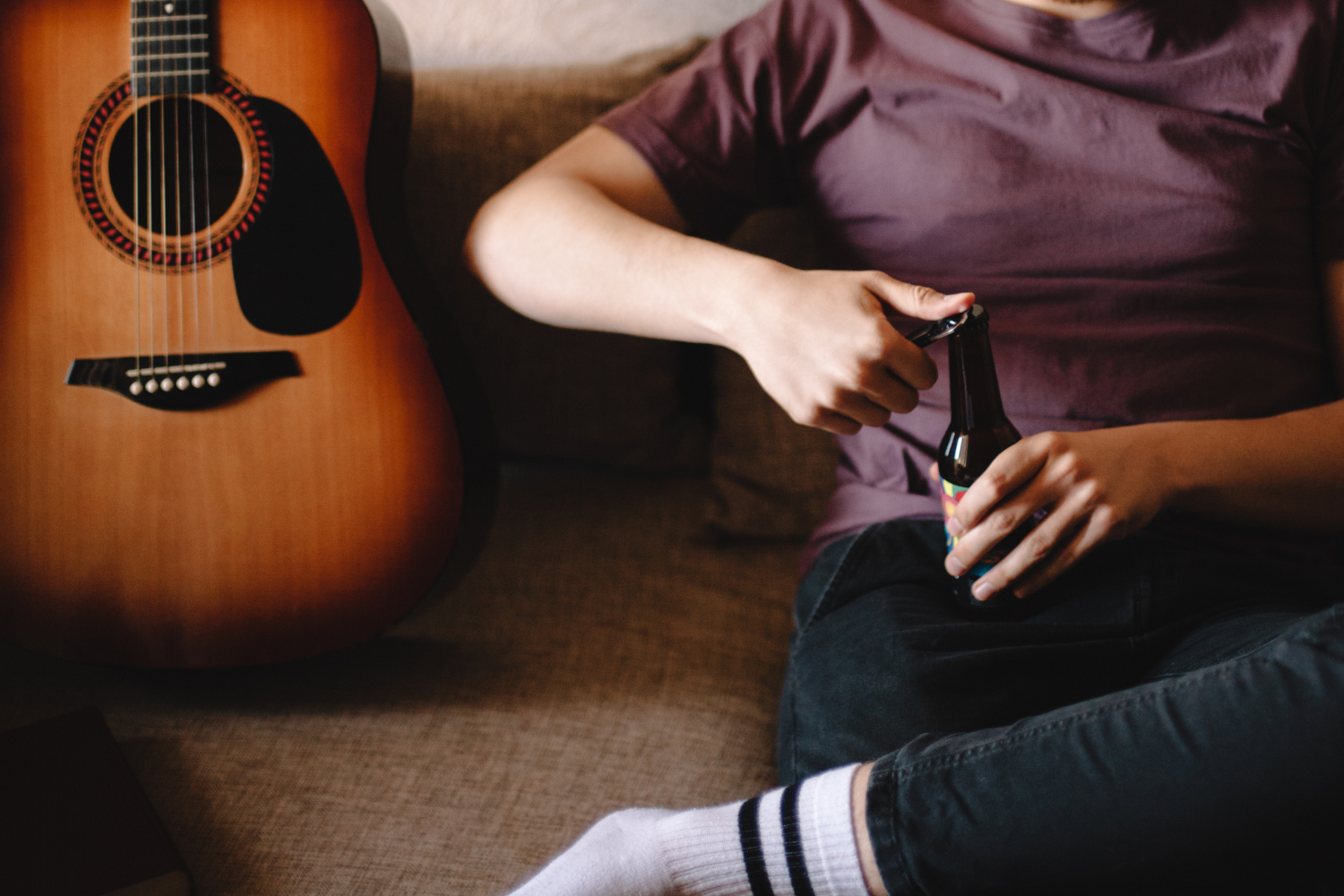 musician opens bottle of beer on couch next to guitar