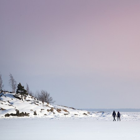 Two figures walking across a wintry landscape, with a pink-blue sky in the background. We look at how many minutes you should spend outside during the winter.
