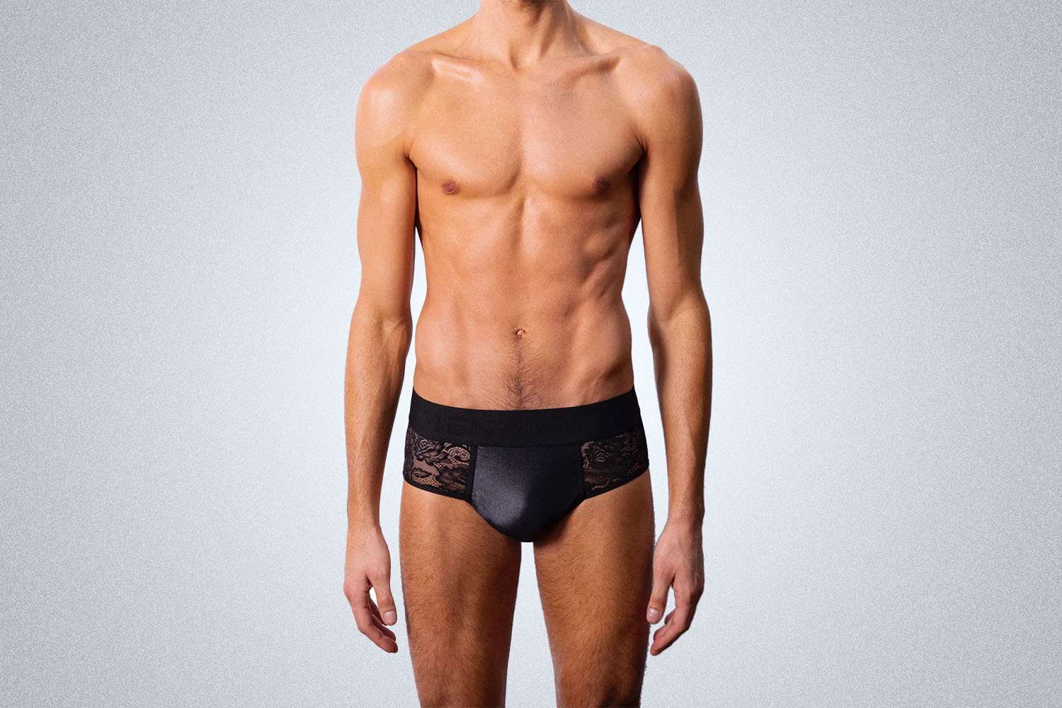 a male model in a pair of lace underwear from Menagerie on a grey background