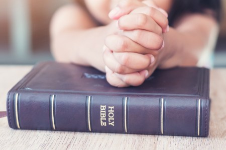 child's hands folded in prayer over bible