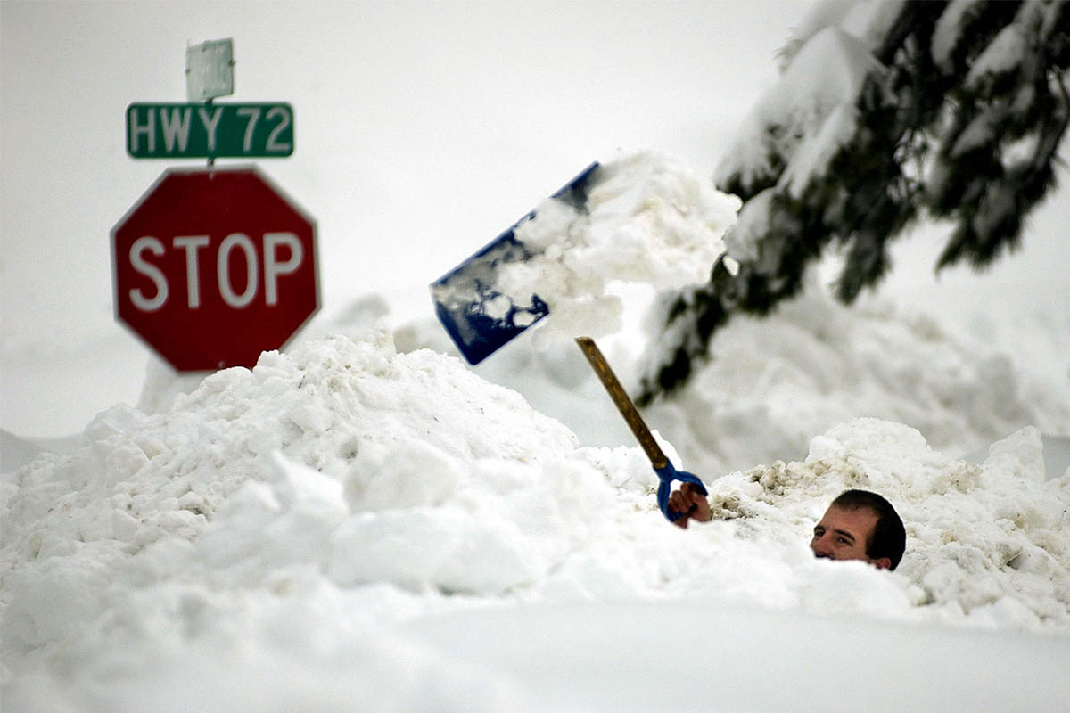 A man tossing snow over his head with a shovel. Here are the best stretches after shoveling snow.