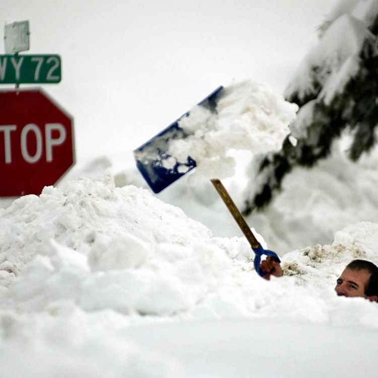 A man tossing snow over his head with a shovel. Here are the best stretches after shoveling snow.