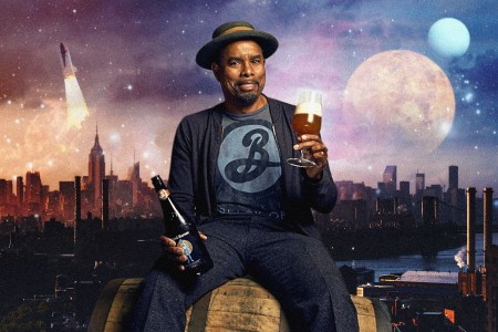Garrett Oliver of Brooklyn Brewery holds a glass of beer while seated on a cask