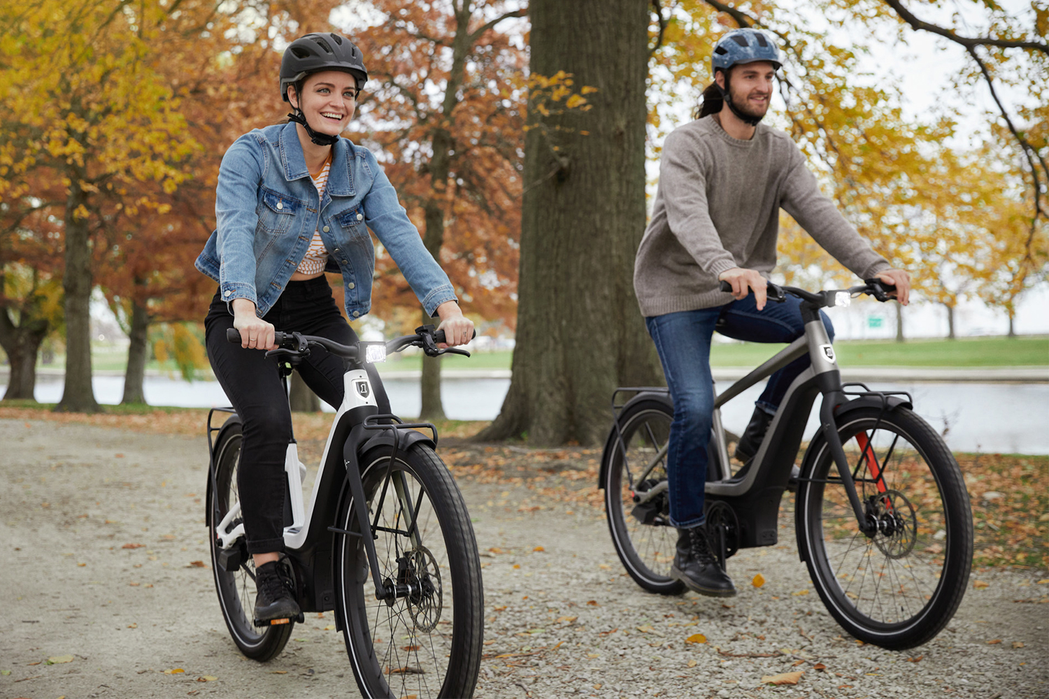 A woman and a man riding two electric bikes from Harley-Davidson's new offshoot company Serial 1 down a street in autumn