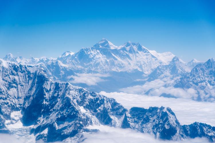 Snow capped Mount Everest photographed from far away overlooking other peaks under a blue sky