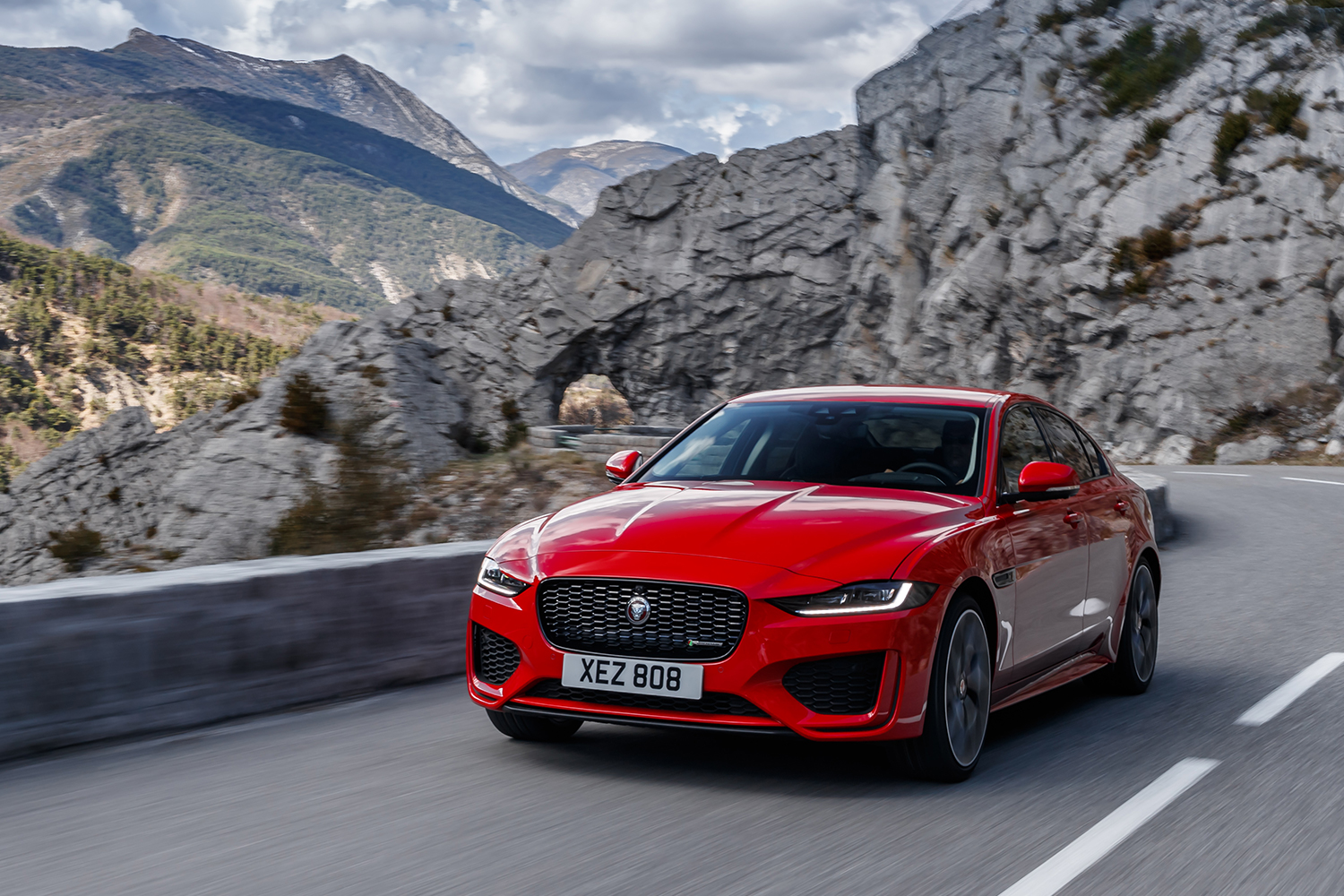 A red Jaguar XE driving on the right side of the road through the mountains