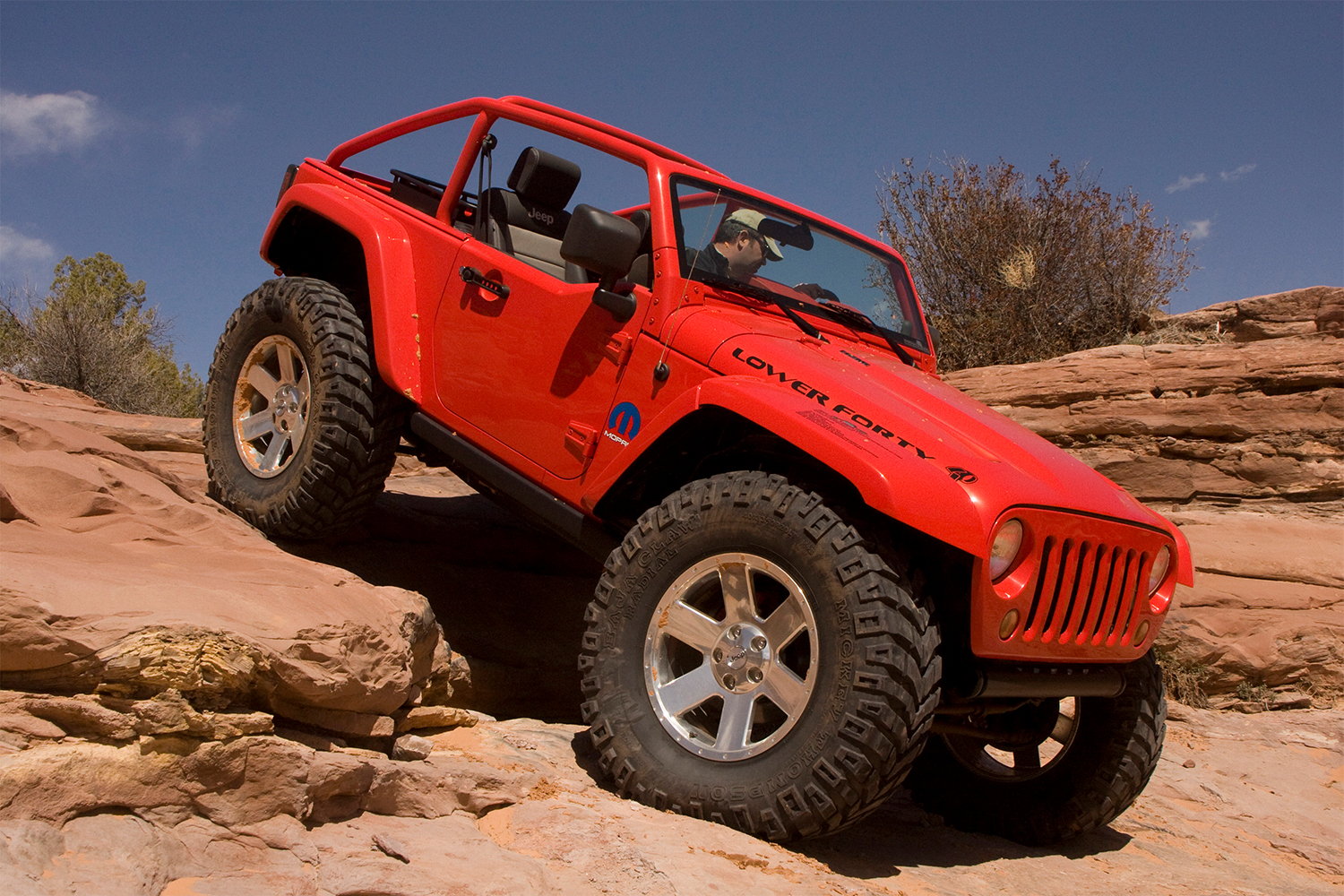 A red Jeep Wrangler with huge tires rock crawling at the Easter Jeep Safari
