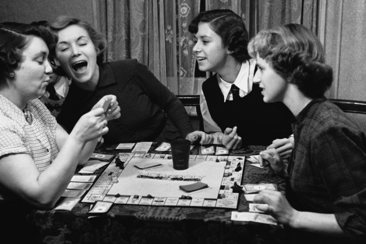 Black and white photo of actress Veronica Hurst (second from left) playing Monopoly with family members.