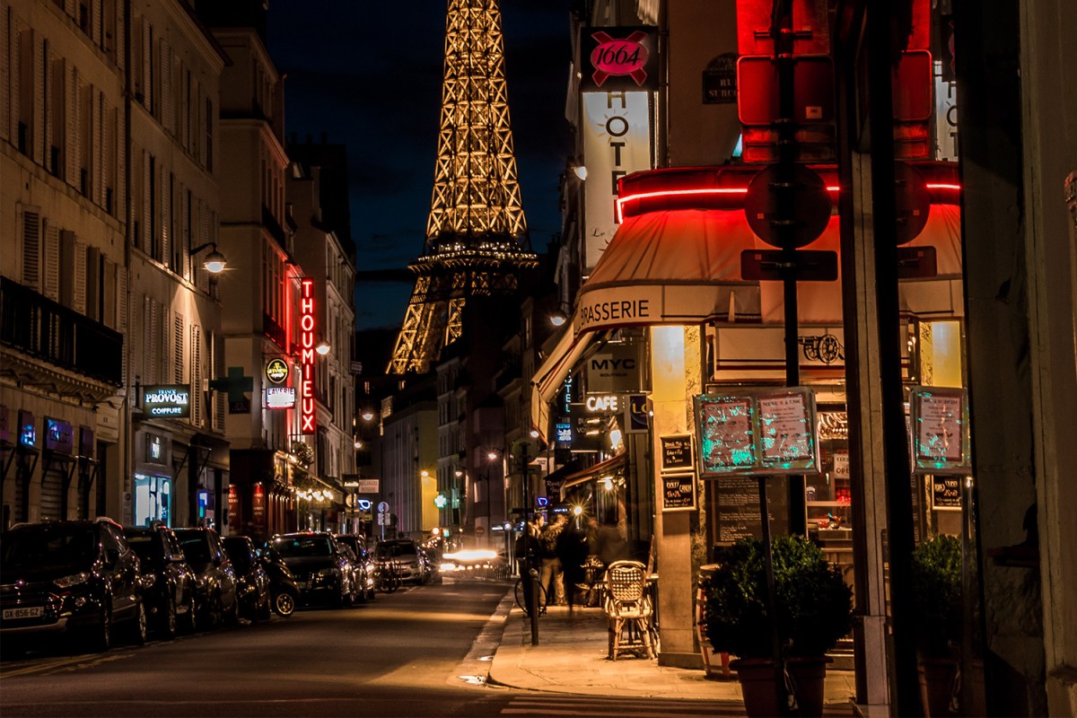 The corner of a street in Paris at night with a view of the Eiffel Tower in the background