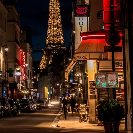 The corner of a street in Paris at night with a view of the Eiffel Tower in the background