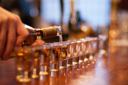 Alcohol being poured into a line of shot glasses set up on a bar