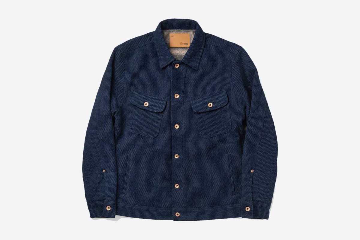 The blue Taylor Stitch Long Haul Jacket in Indigo Sashiko fabric on a grey background
