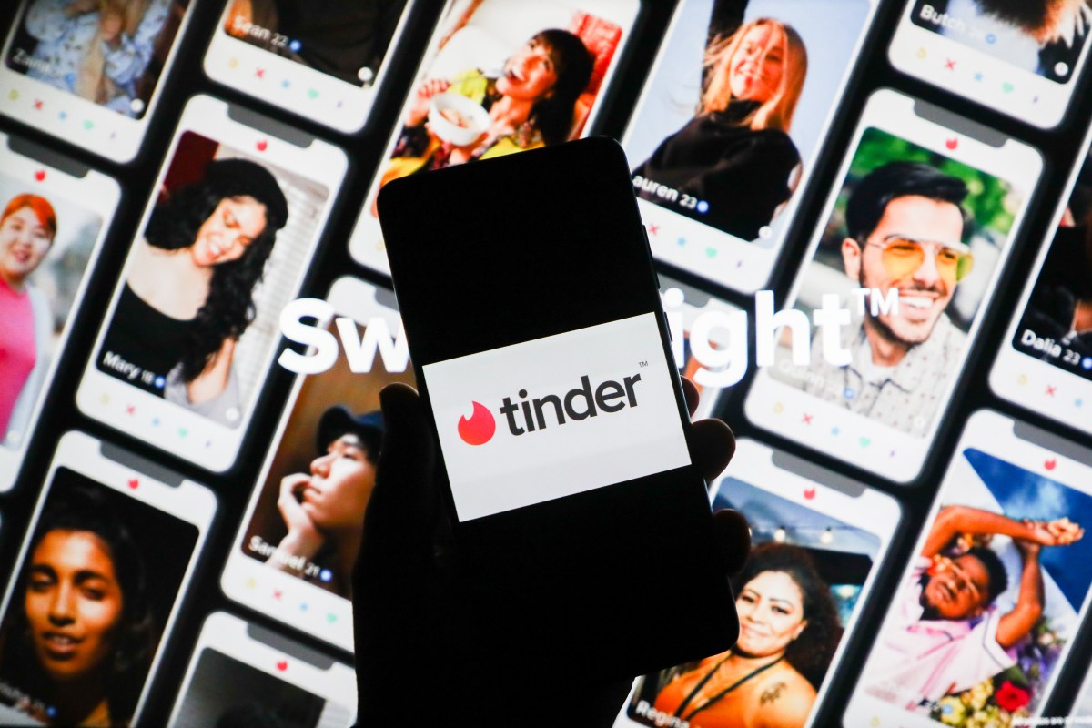 Tinder app logo is displayed on a mobile phone screen photographed on Tinder website background.