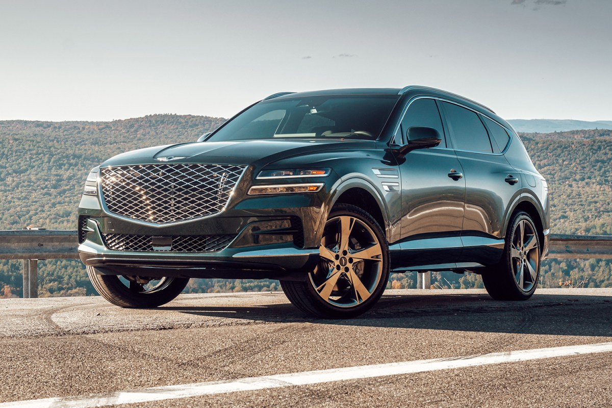 The 2021 Genesis GV80 SUV in green stands still on a road with hills behind