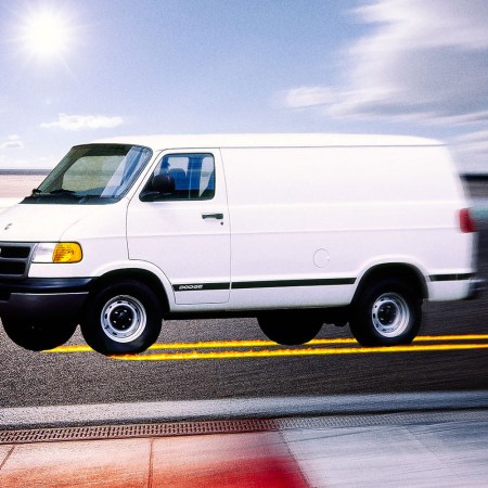 A white Dodge B-series van racing down a track with flames running behind