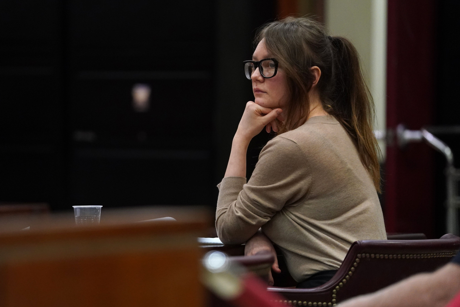anna delvey sits in a court room resting her chin on her hand