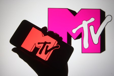 A hand holding up a smartphone with the MTV logo and the MTV logo behind in pink