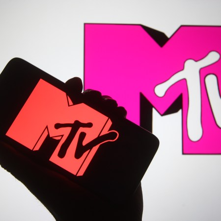A hand holding up a smartphone with the MTV logo and the MTV logo behind in pink