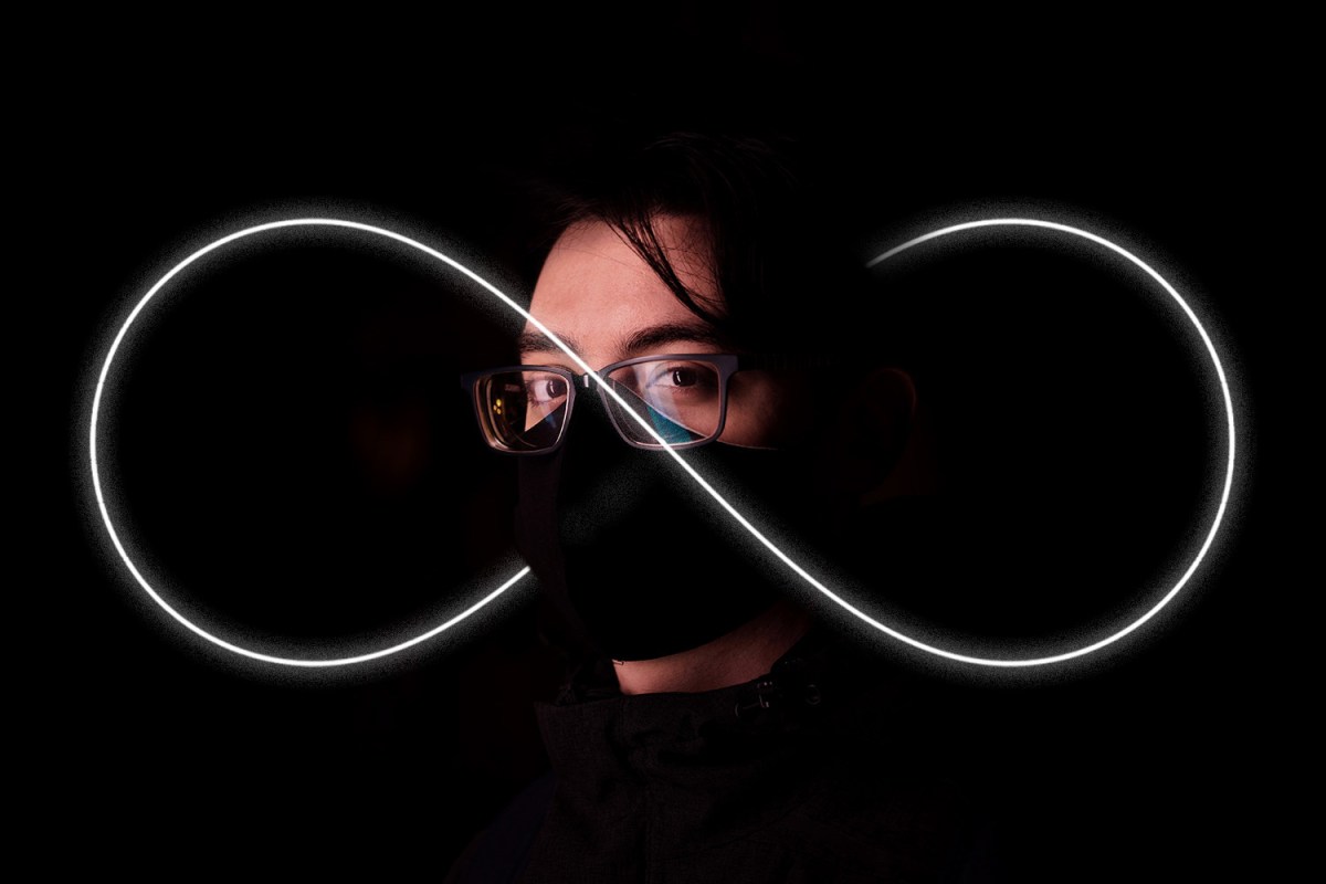 an iluminated infinity symbol backlights a man wearing a mask