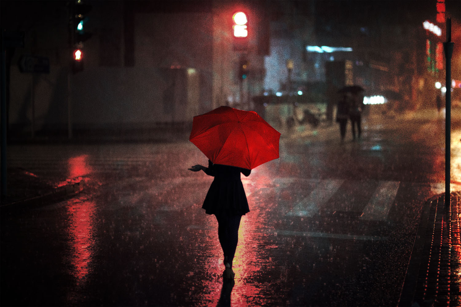 A woman in Shanghai, China appears in silhouette as she crosses a rainy street at night. She holds out her hand under a red umbrella