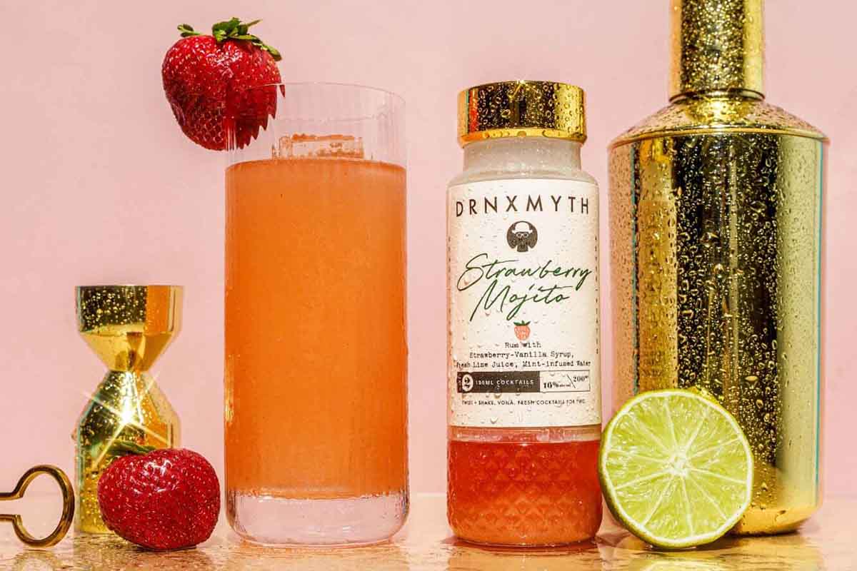 DRNKMYTH strawberry mojito in bottle and glass, along with a shaker, jigger and fruit