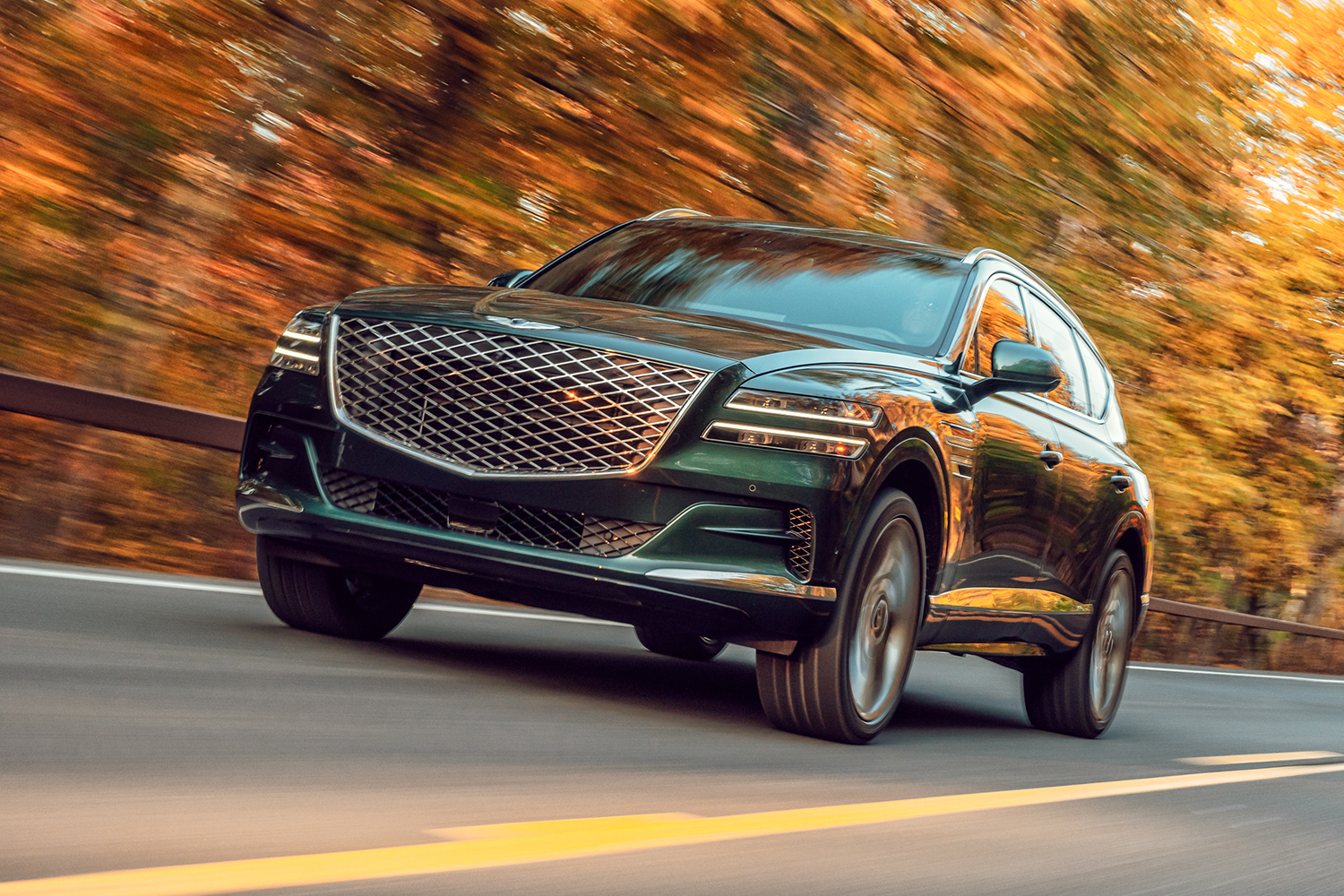 The 2021 Genesis GV80 SUV driving past trees with fall foliage