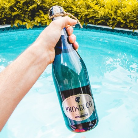man holding bottle of prosecco with a pool in the background