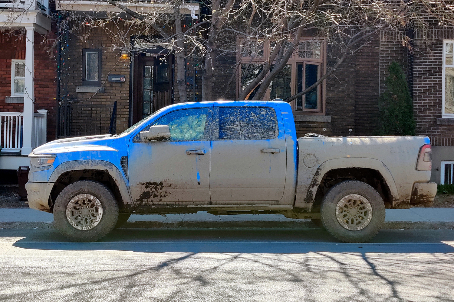 A blue 2021 Ram 1500 TRX pickup truck covered in mud parked on a city street