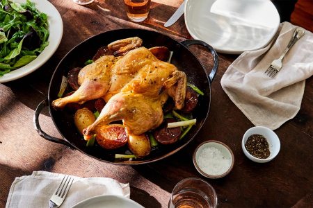 The Smithey Carbon Steel Round Roaster sitting on a table with a chicken and potatoes in it