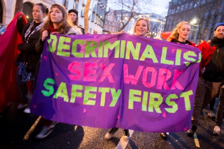 Sex workers joined by members of the public march through central London carrying a purple banner saying, "DECRIMINALIZE SEX WORK SAFTEY FIRST"