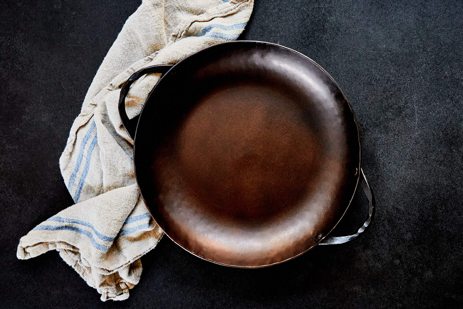 The Carbon Steel Round Roaster Pan from Smithey sitting next to a towel
