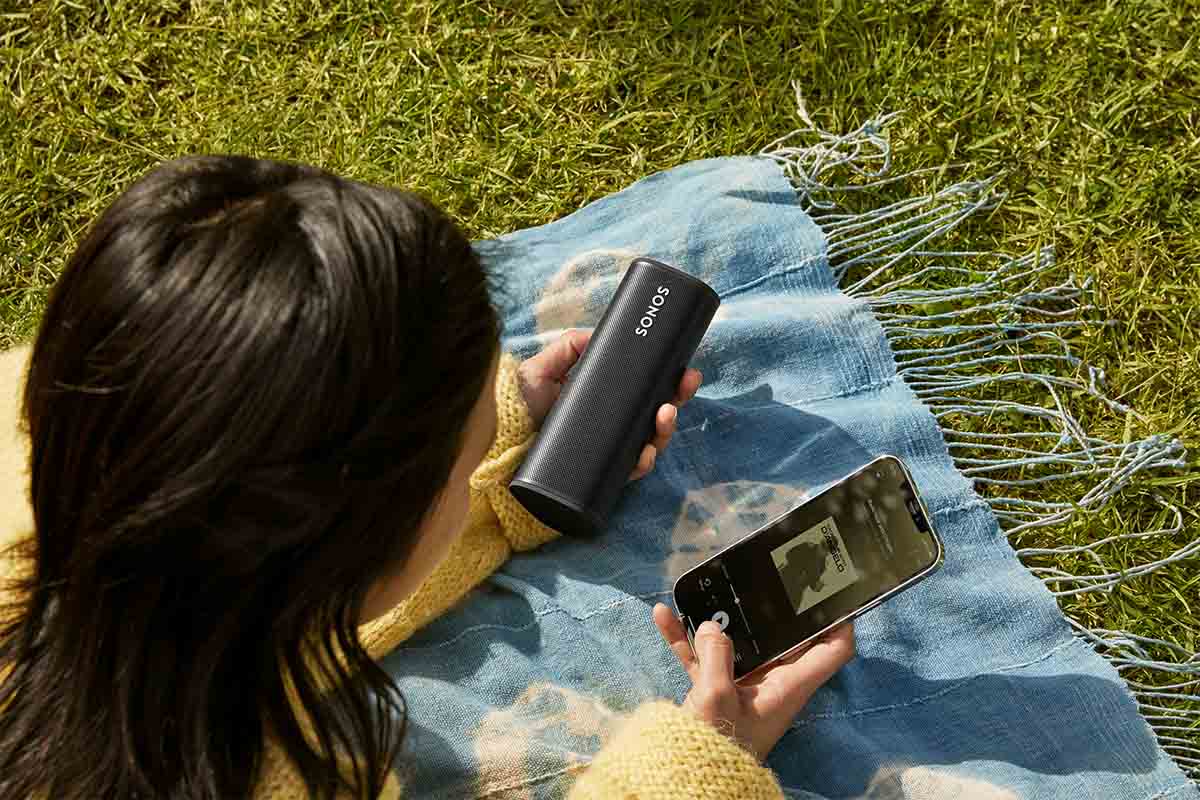 A woman pairing her phone with a Sonos Roam while sitting on a blanket in a park