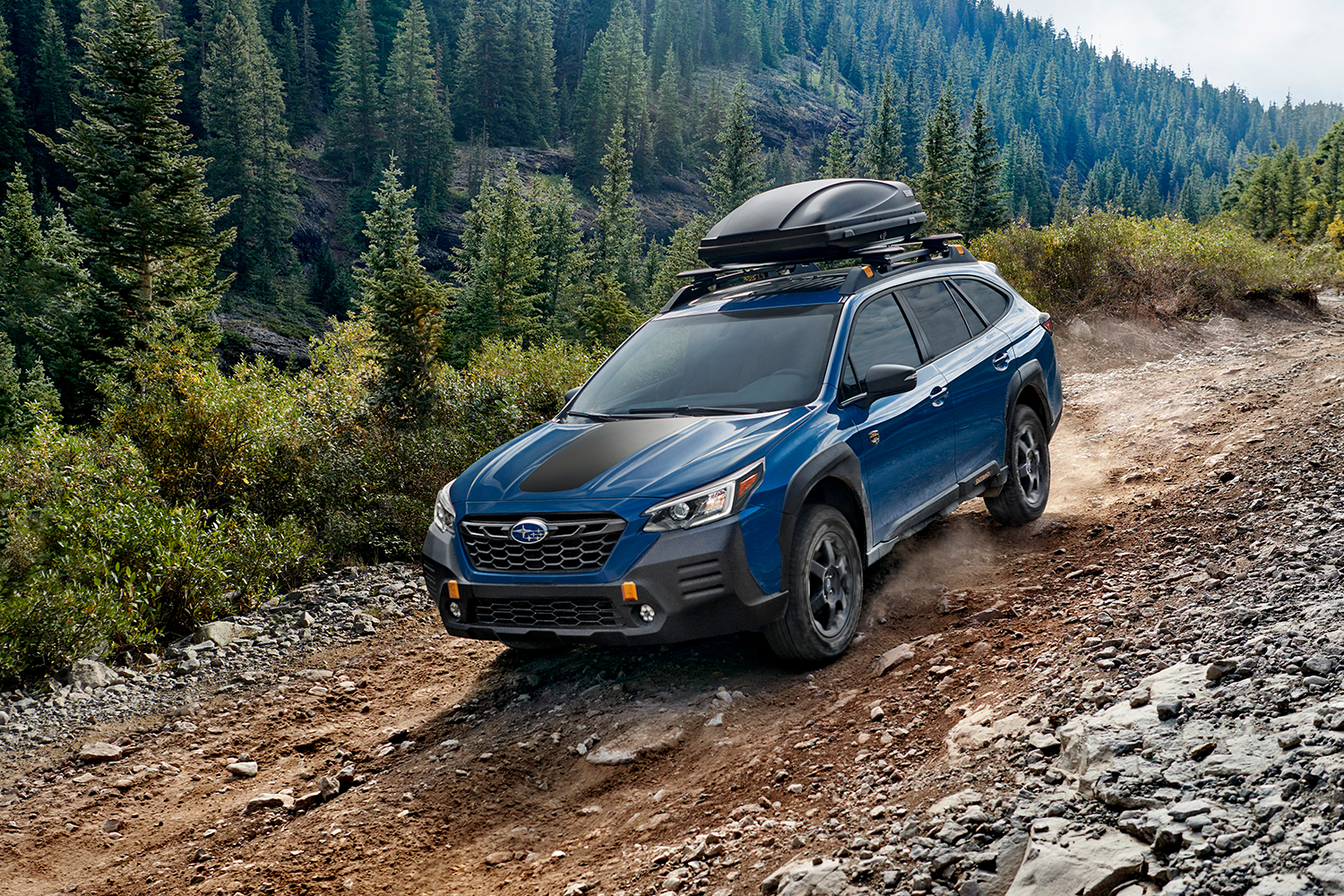 A blue 2022 Subaru Outback Wilderness SUV driving down an off-road trail