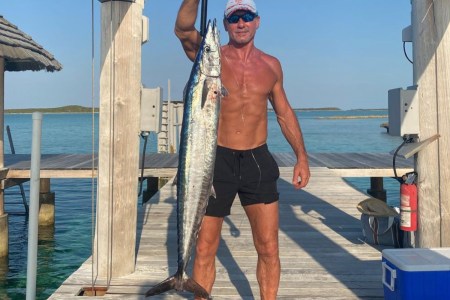 A photo of a shirtless Tim McGraw holding up a large fish on a dock