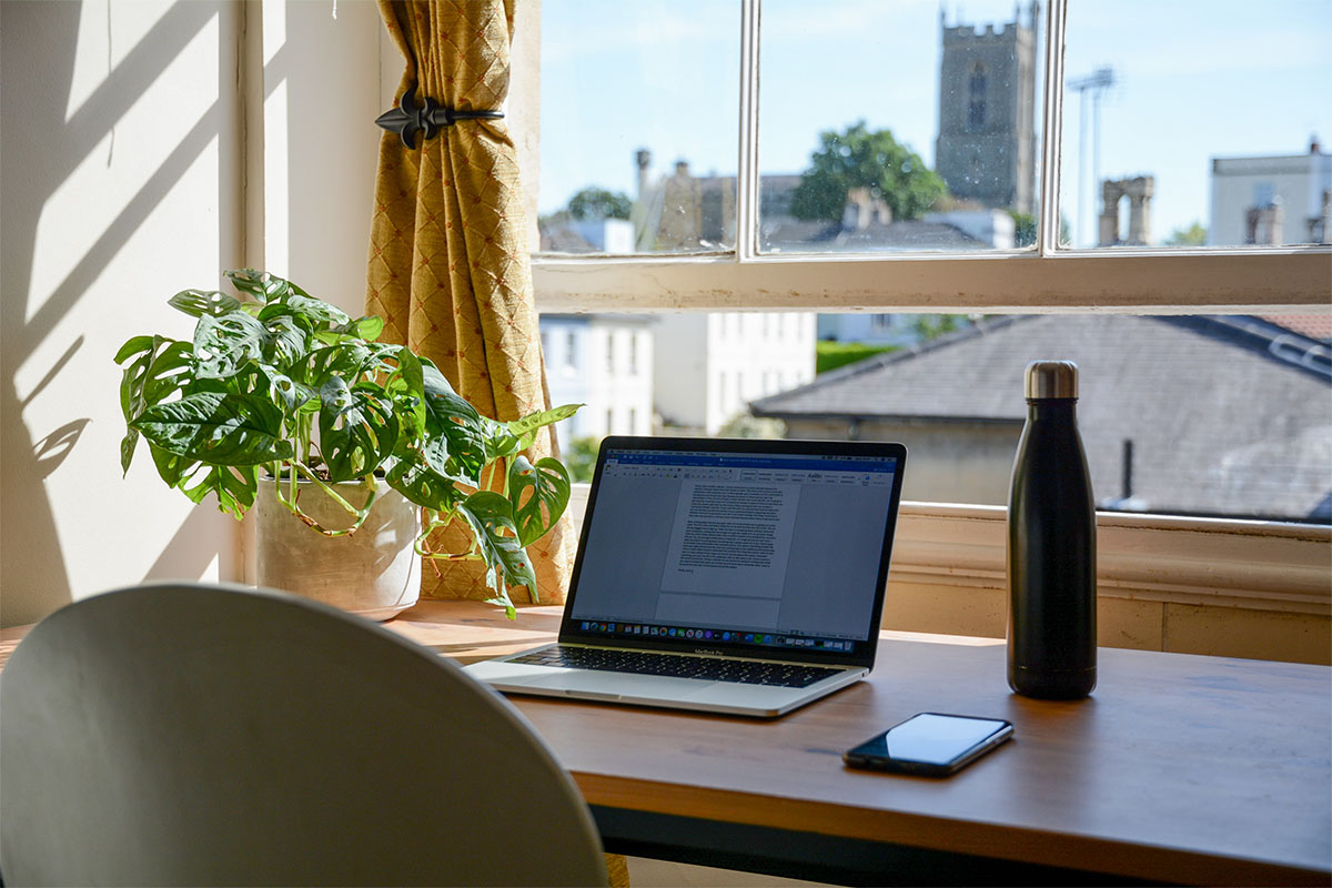 A laptop computer sitting on a desk by a window in a home
