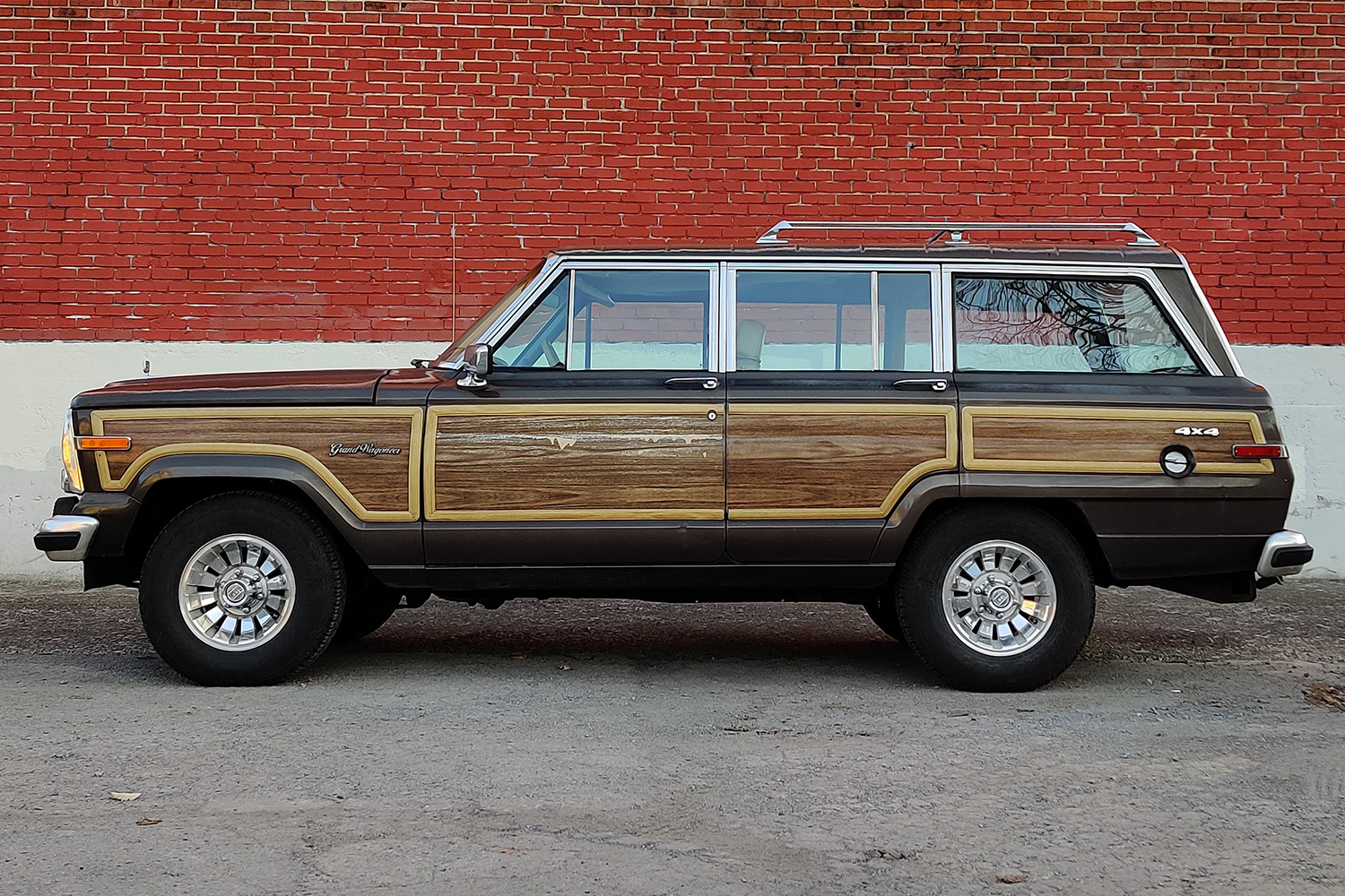 The side profile of a 1987 Jeep Grand Wagoneer against a red brick wall