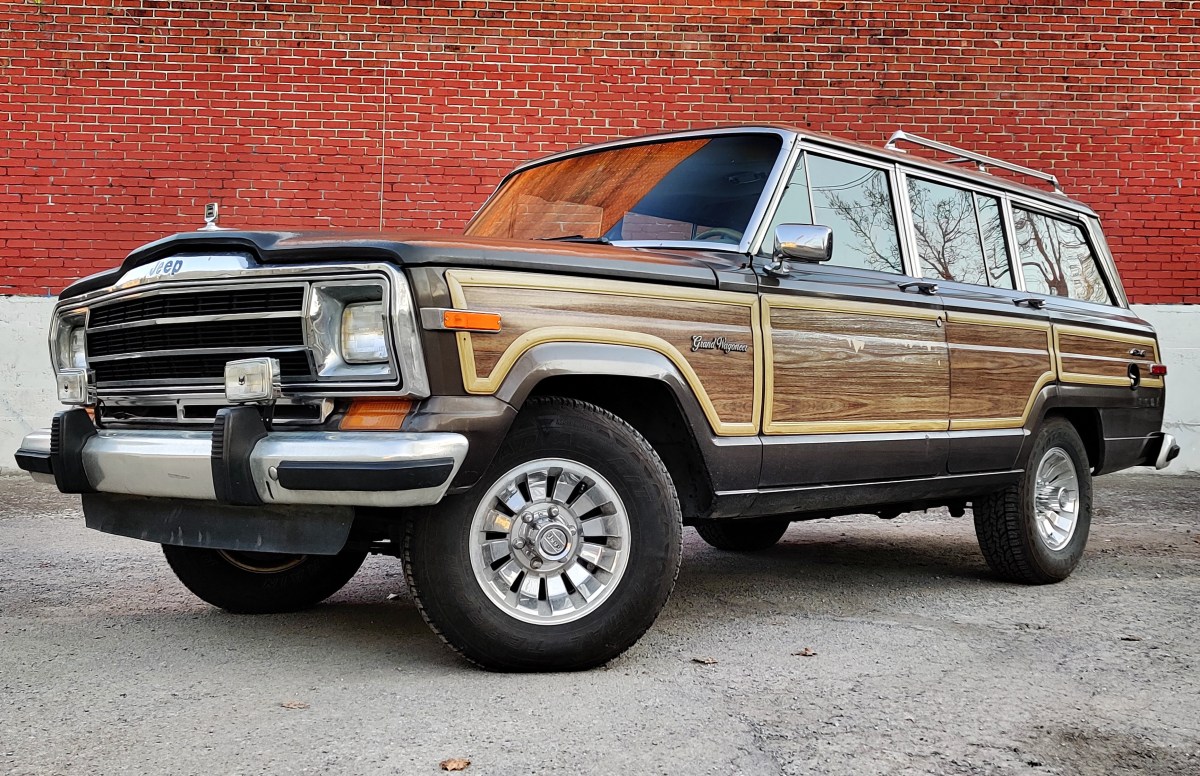 A 1987 Jeep Grand Wagoneer sitting in front of a red brick wall