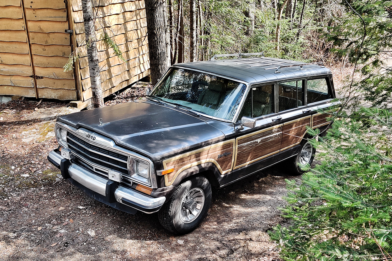 A 1987 Jeep Grand Wagoneer next to a cabin in the woods
