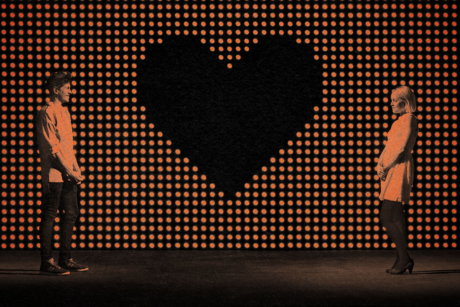 Two people stand far apart from each other on either side of a giant black heart background
