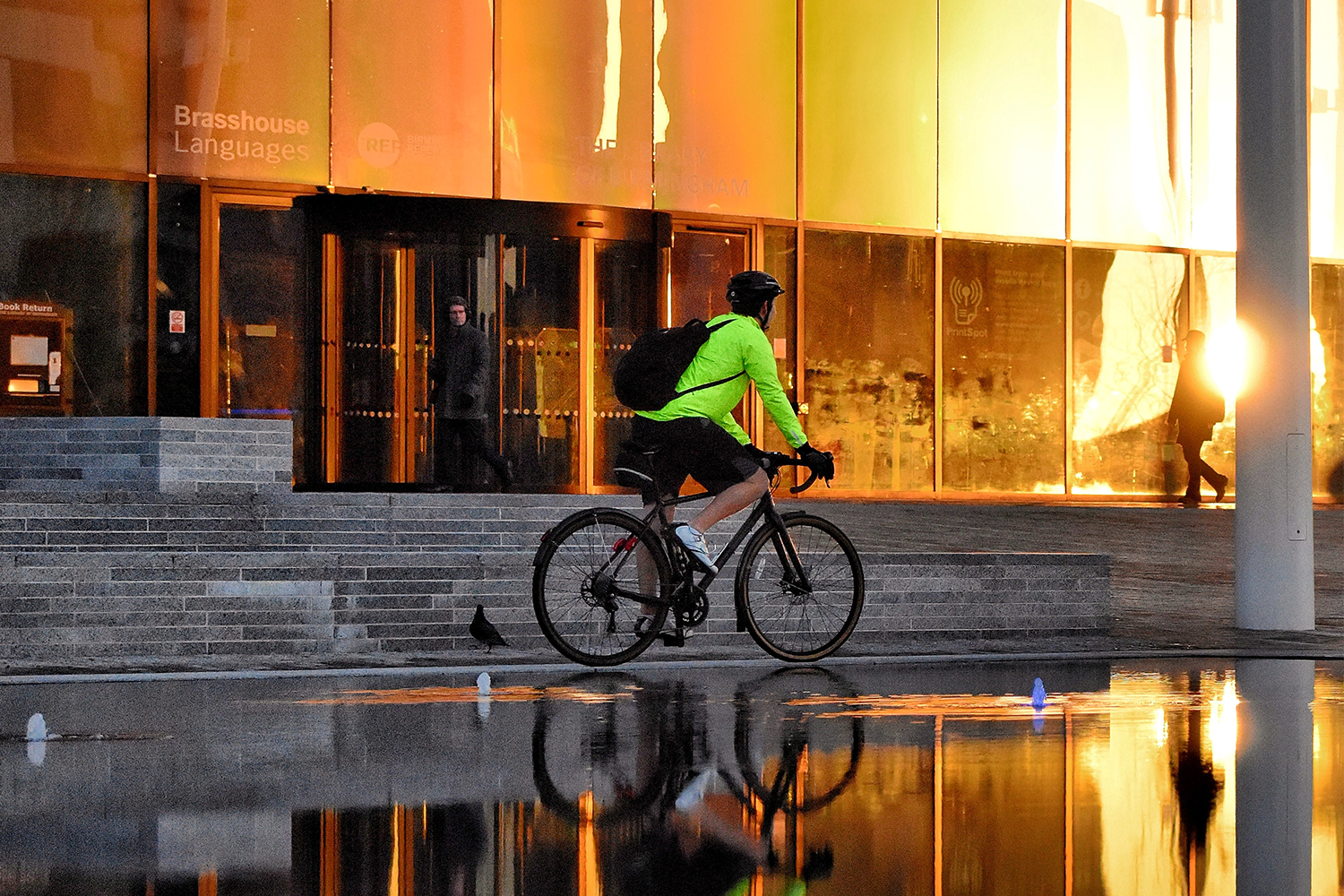 A bike commuter in a fluorescent green jacket biking at sunrise