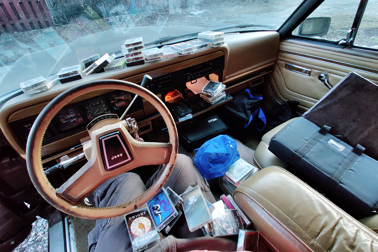 The front two seats of a 1987 Jeep Grand Wagoneer with a bunch of cassette tapes