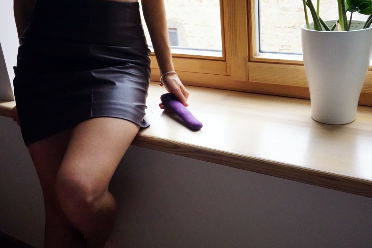 Woman leaning against windowsill holding sex toy